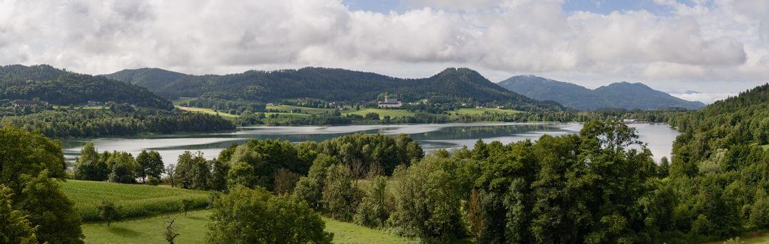 Aussicht auf den St. Georgener See mit grünen Wäldern und Bergen unter bewölktem Himmel